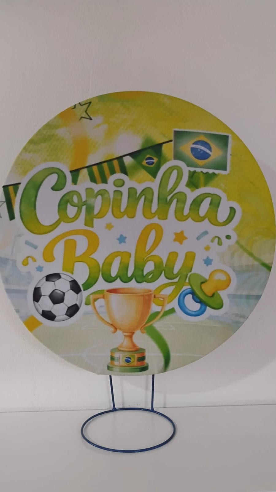 Painel de referência Copinha Baby: a inscrição “Copinha Baby”, uma bola de futebol, uma taça, uma chupeta e as cores do Brasil.