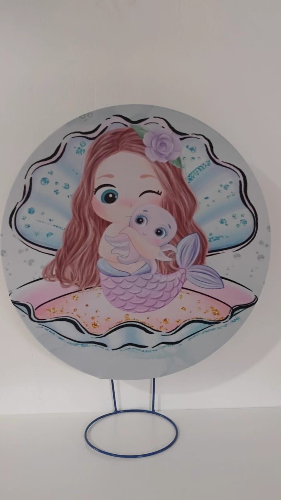 Painel de referência Mamãe e Bebê Sereia: uma bebê-sereia dentro de uma concha, com fundo rosa e detalhes do mar.